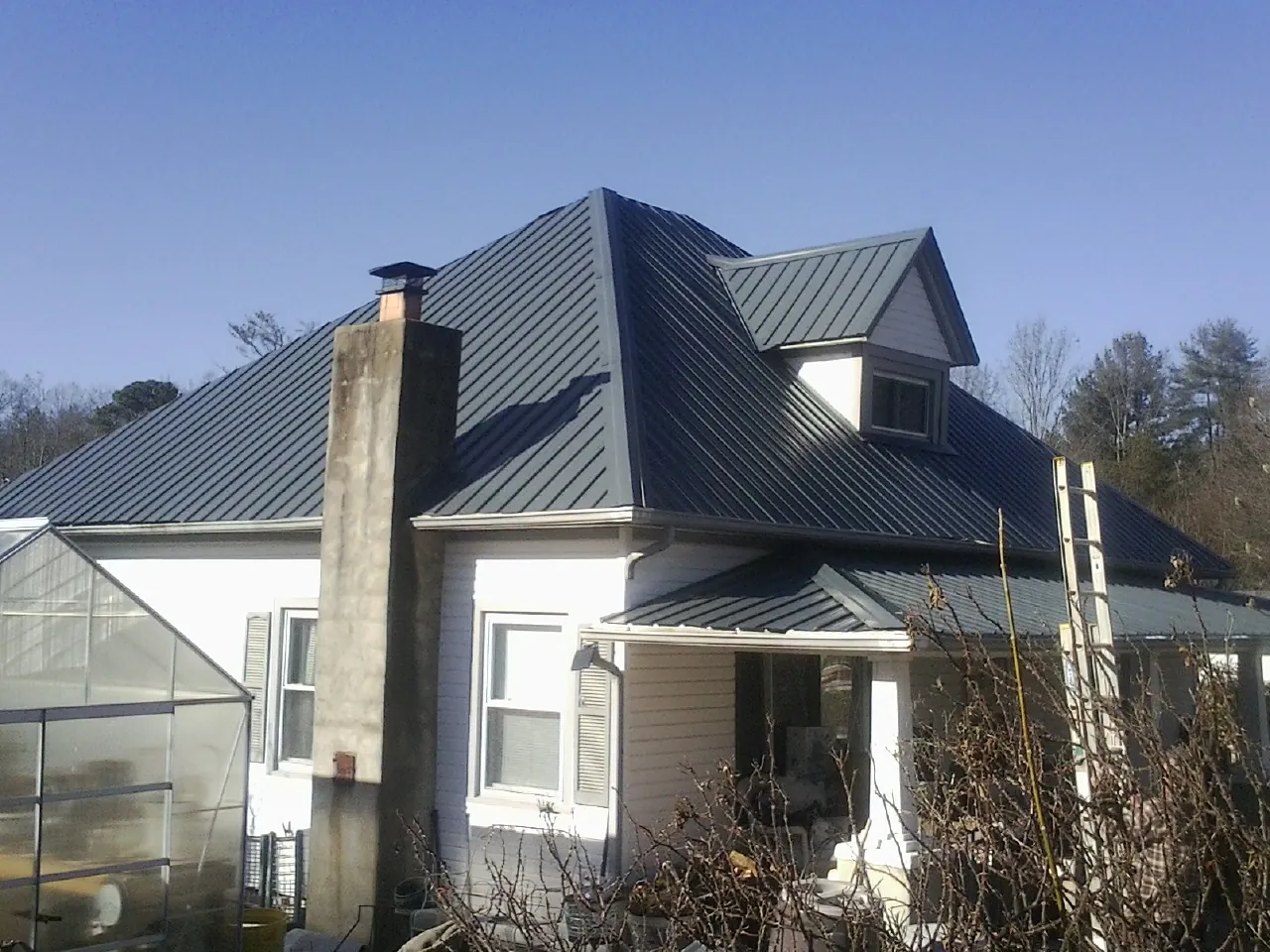 Dark blue standing seam metal roof on a white farmhouse with dormer — Slate & Tile Roof Repair by Roofing Brothers in Wilson