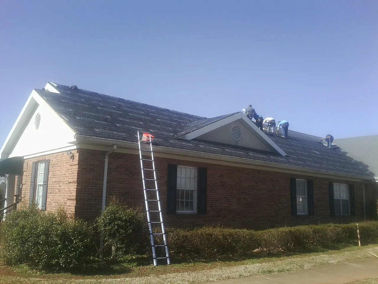 Crew tearing shingles off a brick ranch roof with a ladder set — Emergency Roof Repair work by our crew in Wilson