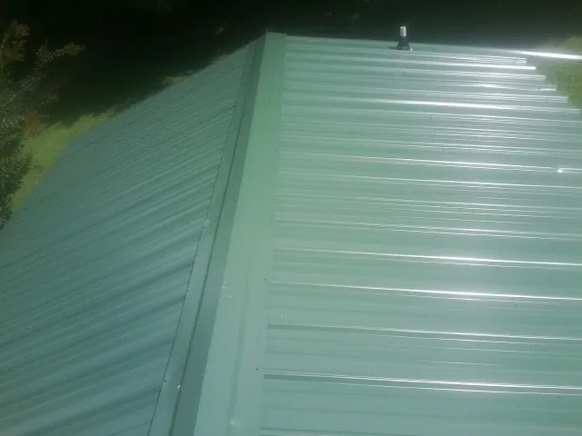 New green metal panels meeting at the ridge of a roof — Flat Roof Repair work by our crew in Wilson