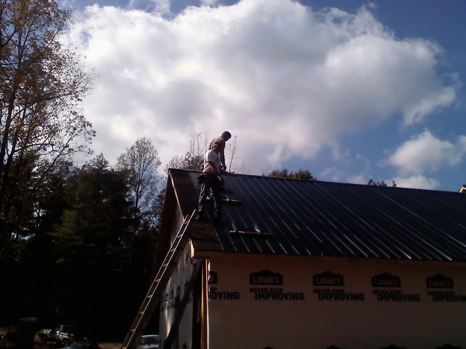 Roofer fastening dark metal panels high against a cloudy sky, from a Roof Inspection job in Wilson